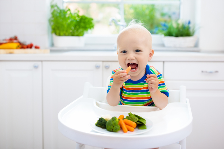 Baby eating vegetables in kitchen. Healthy food.